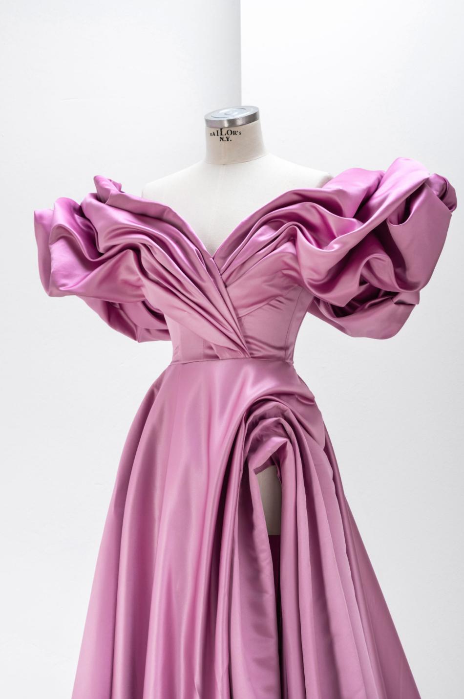 Pink satin off-shoulder A-line gown with voluminous pleated sleeves and a high side slit on a dress form.