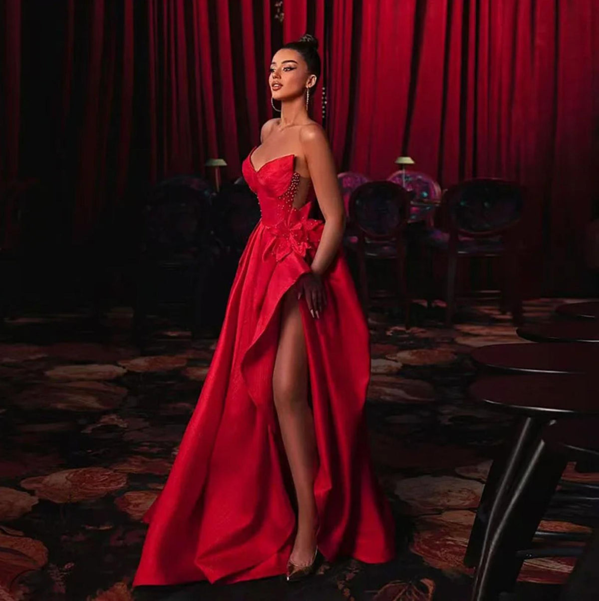 Red satin A-line evening gown with a strapless sweetheart neckline, floral waist detail, and a high leg slit.