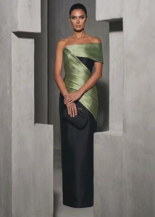 Model in a structured olive green and black satin twill floor-length gown with an asymmetrical off-shoulder neckline.