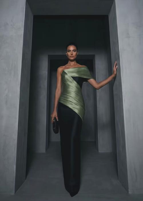 Model wearing a structured olive green and black satin twill floor-length gown with an elegant one-shoulder bodice.