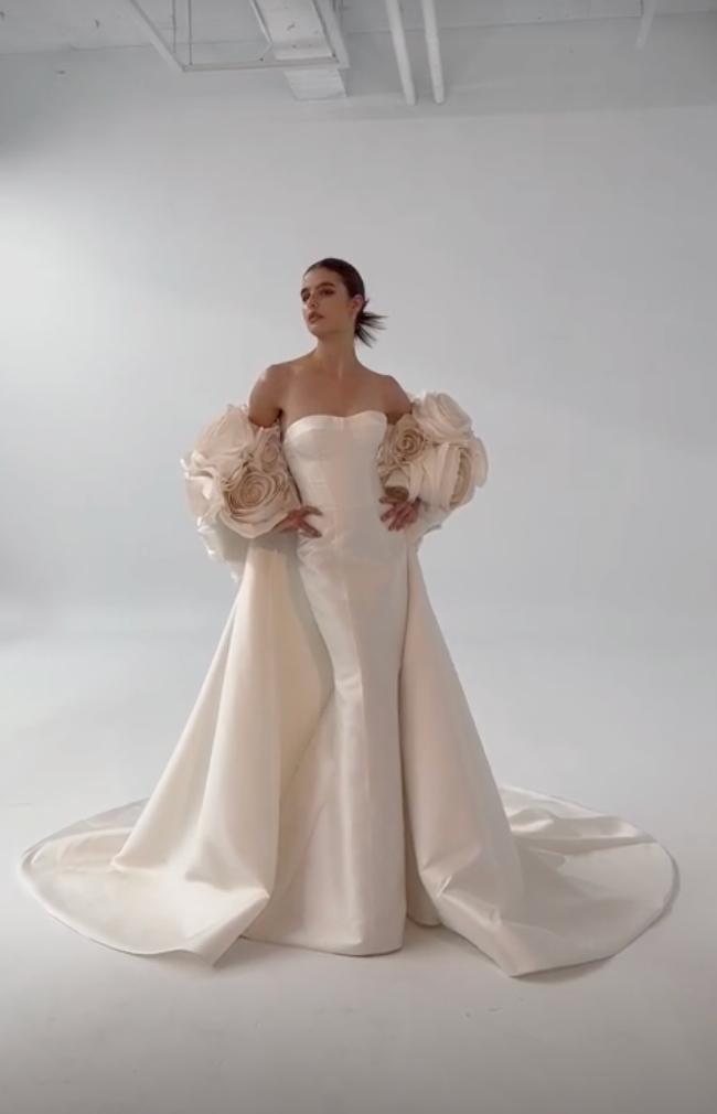 White satin mermaid gown with sweetheart neckline and dramatic 3D floral puff sleeves on a studio background.