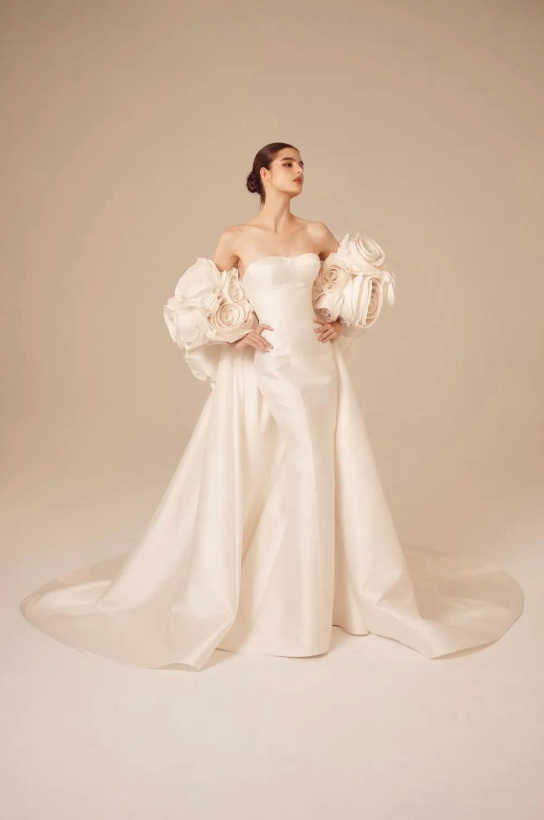 Elegant ivory satin mermaid gown featuring a sweetheart neckline and dramatic 3D floral appliqué sleeves.