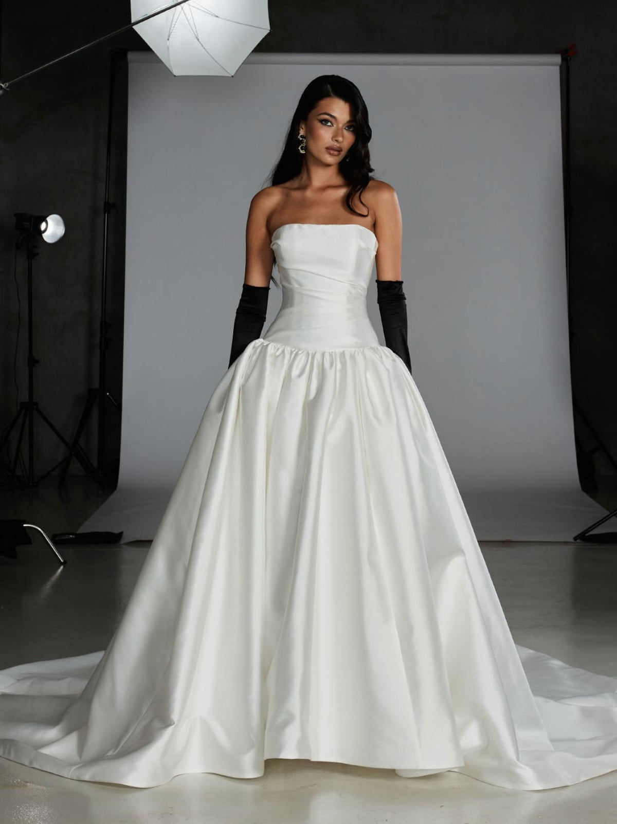 Strapless white Mikado ball gown with a ruched bodice, drop waist, and voluminous skirt, styled with black opera gloves.