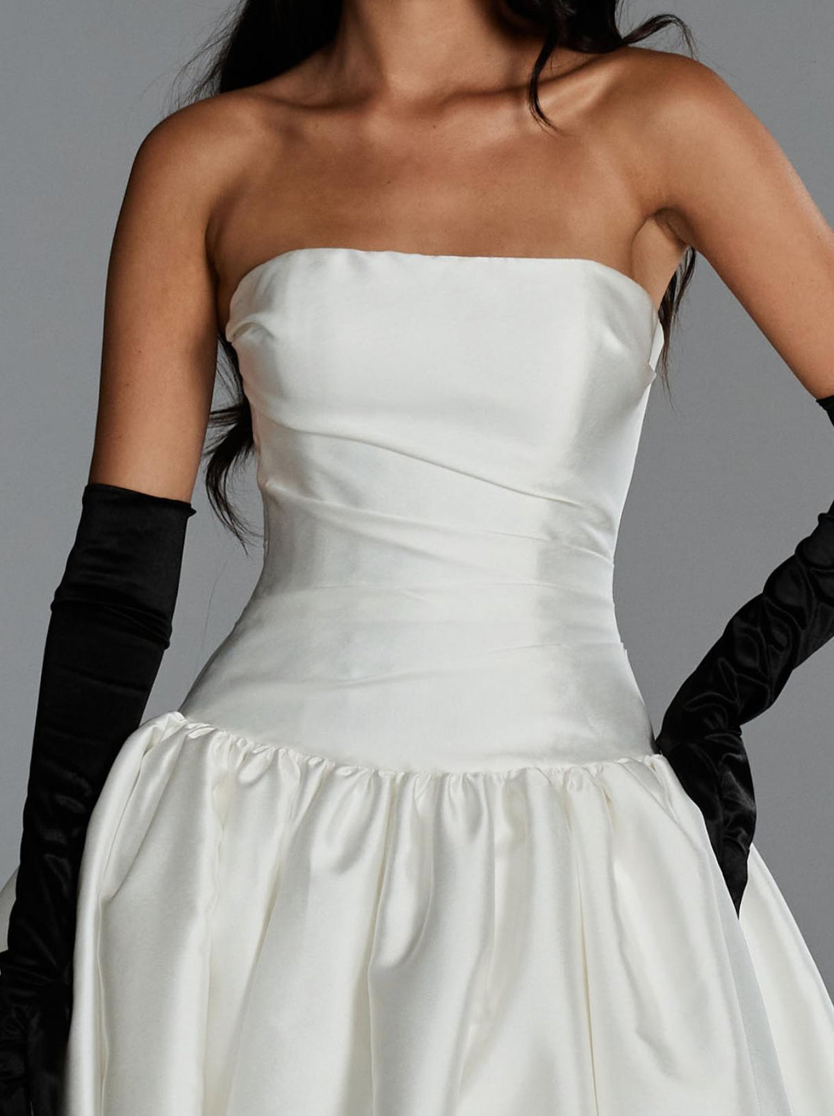 White strapless Mikado ball gown with a ruched bodice, drop waist, and voluminous skirt, styled with black satin gloves.