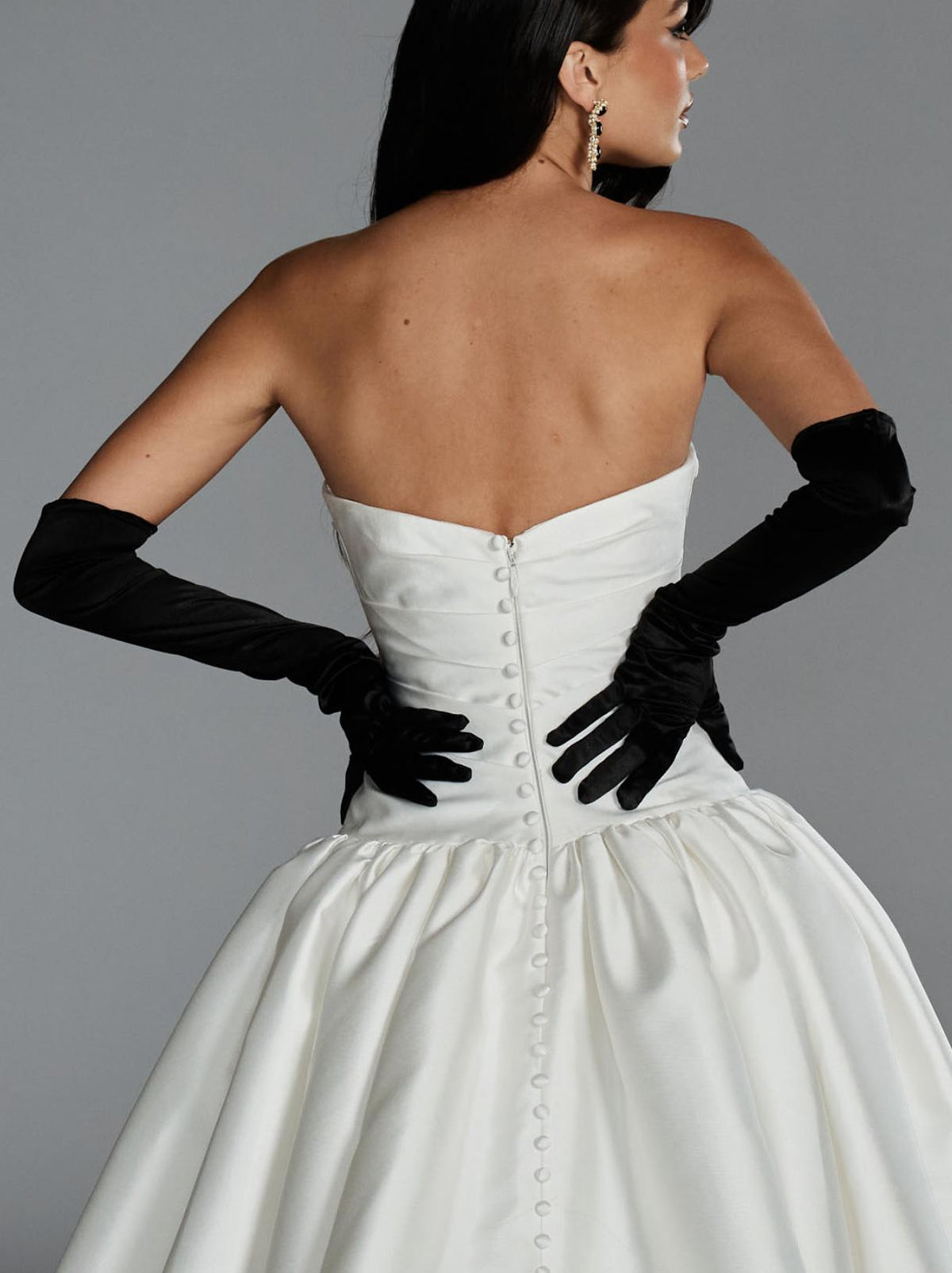 Back view of a white Mikado ball gown with a button-up strapless bodice and voluminous skirt, styled with black opera gloves.