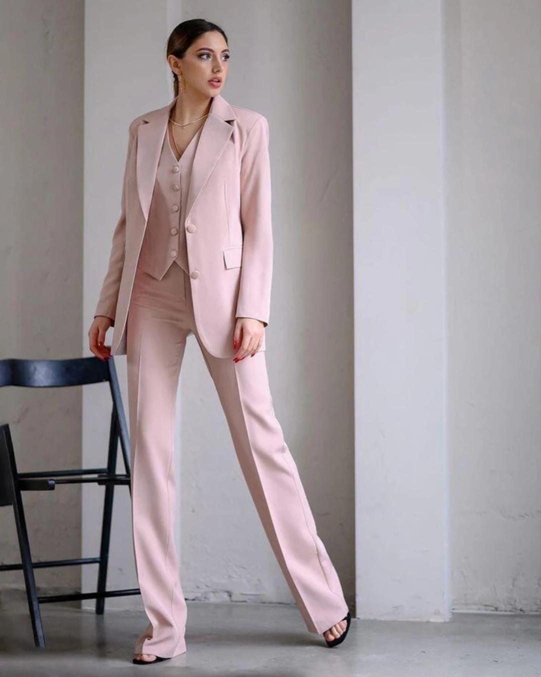 Woman wearing a pink three-piece serge suit with a single-breasted blazer, buttoned vest, and wide-leg trousers.