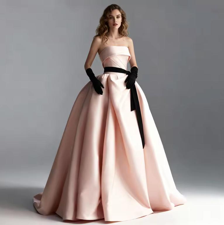 Strapless light pink satin A-line ball gown with a black ribbon waist, pleated bodice, and matching black opera gloves.