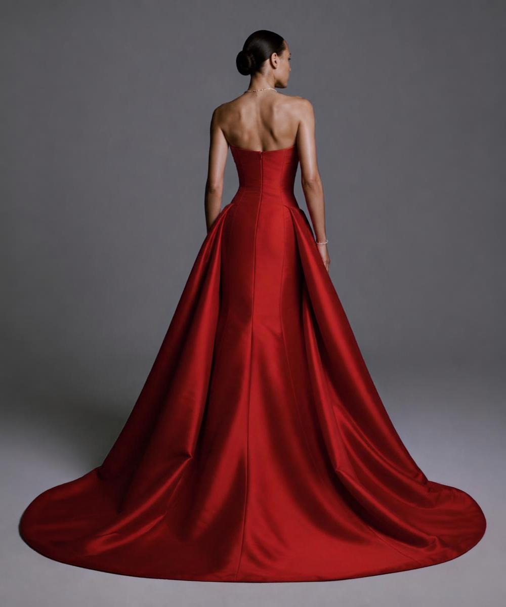 Red strapless mikado gown featuring a structured bodice, sculptural overskirt, and a dramatic floor-length train.