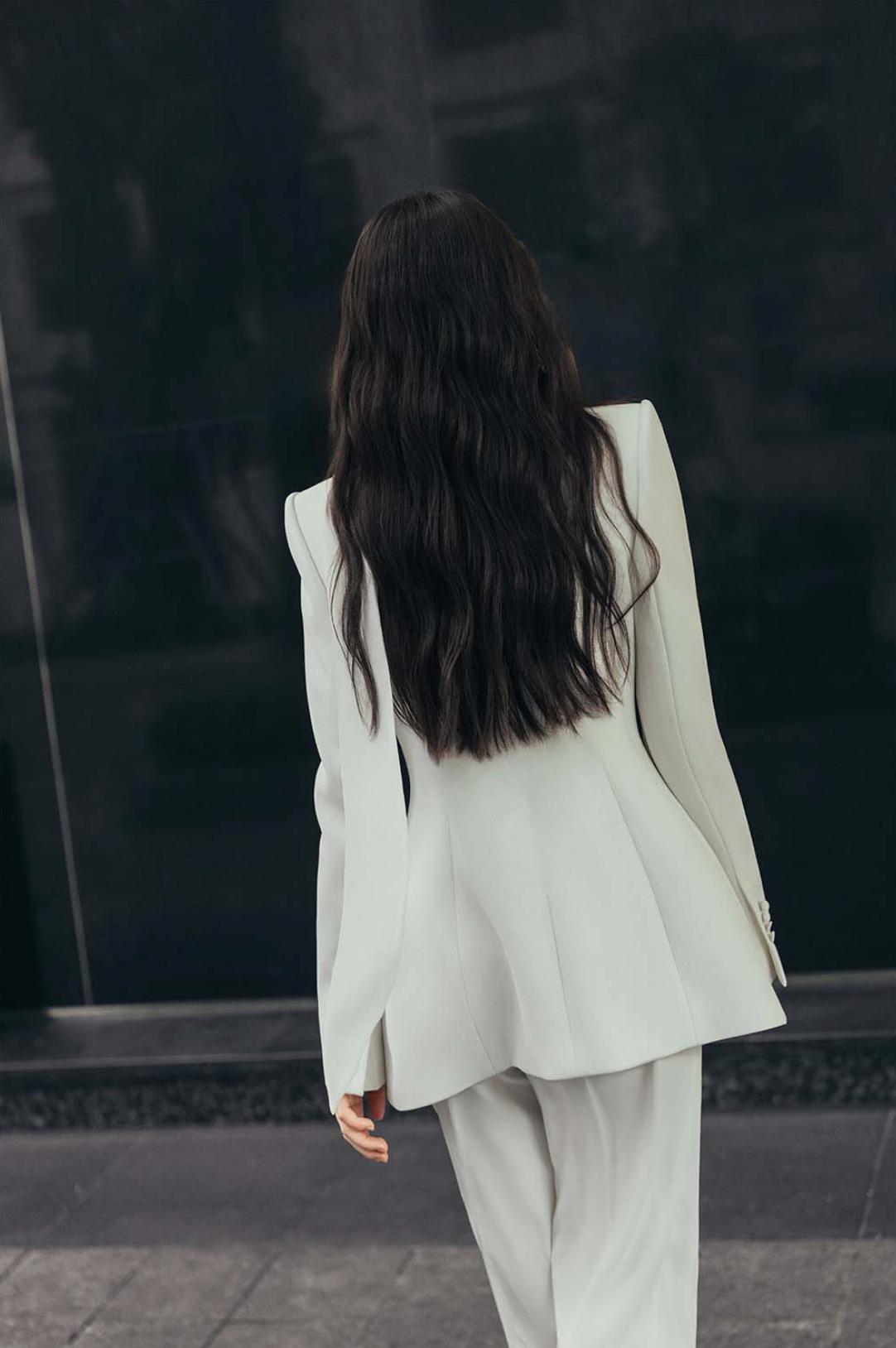 Woman wearing a tailored white Italian satin suit set with a structured one-button jacket and matching trousers.