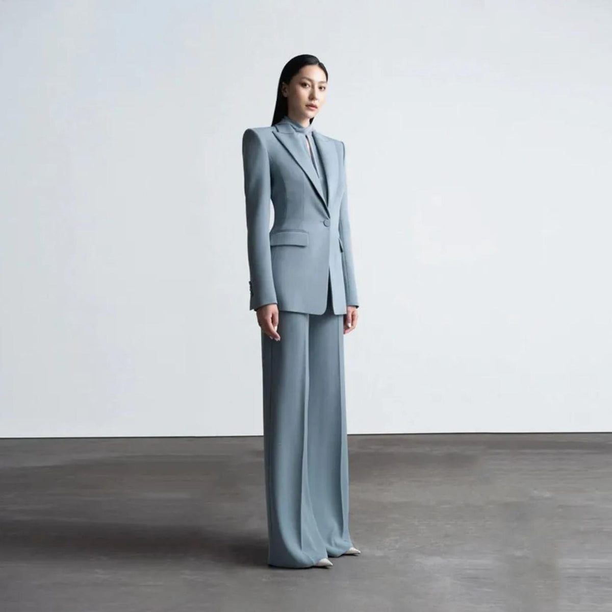 Woman wearing a blue Italian satin suit set with a sleek one-button jacket and tailored wide-leg trousers.