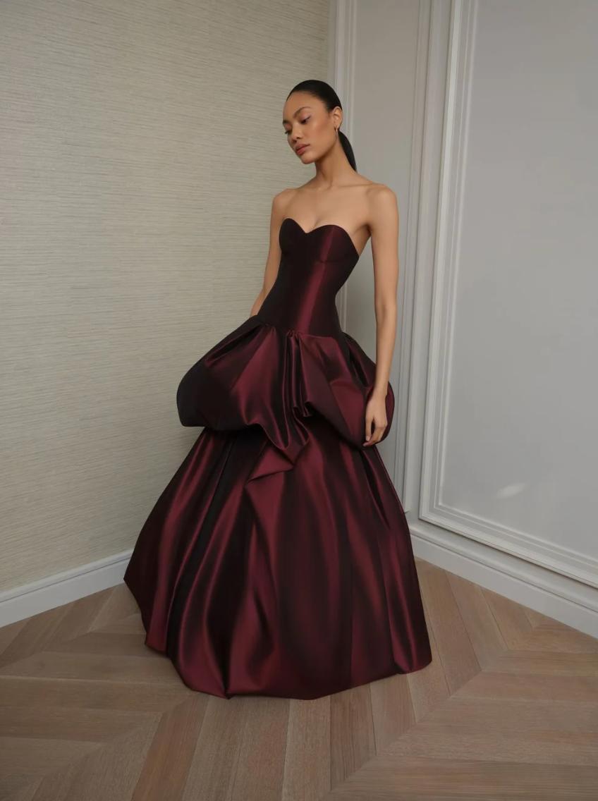 Strapless burgundy silk taffeta ball gown with a structured corseted bodice and dramatic drop-waist tiered skirt.