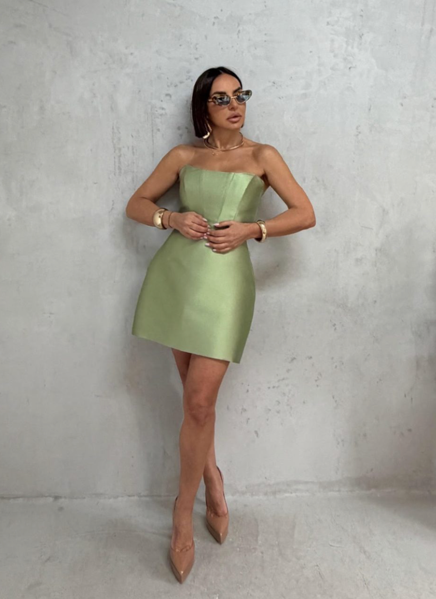 Woman wearing a sage green strapless satin mini dress with an architectural silhouette and polished finish.