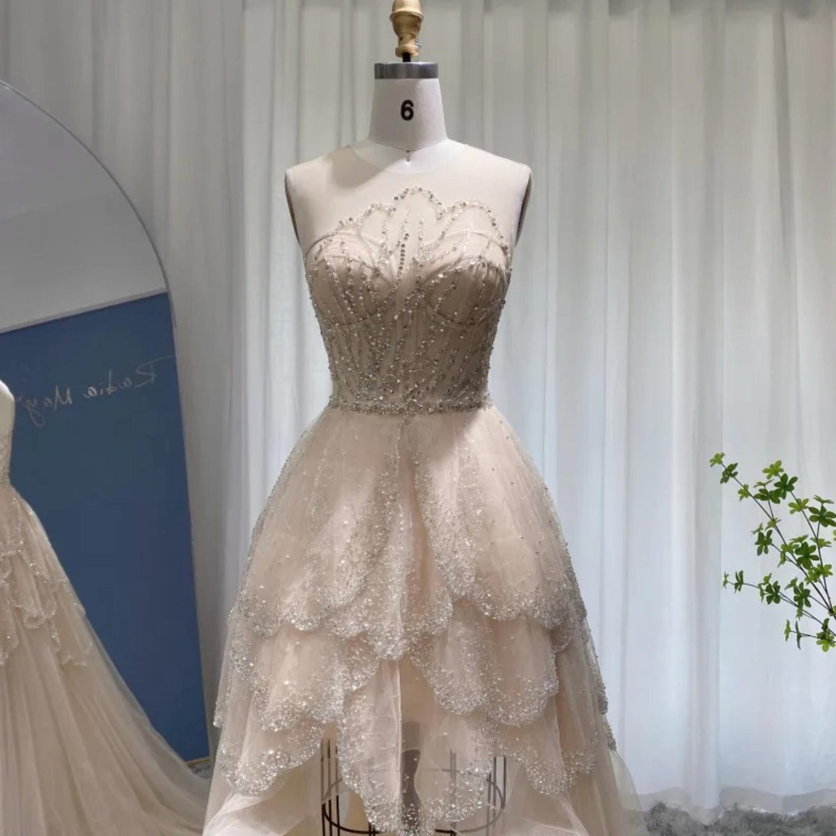 Champagne high-low gown with beaded bodice, scalloped neckline, and tiered tulle ruffles on a dress form.