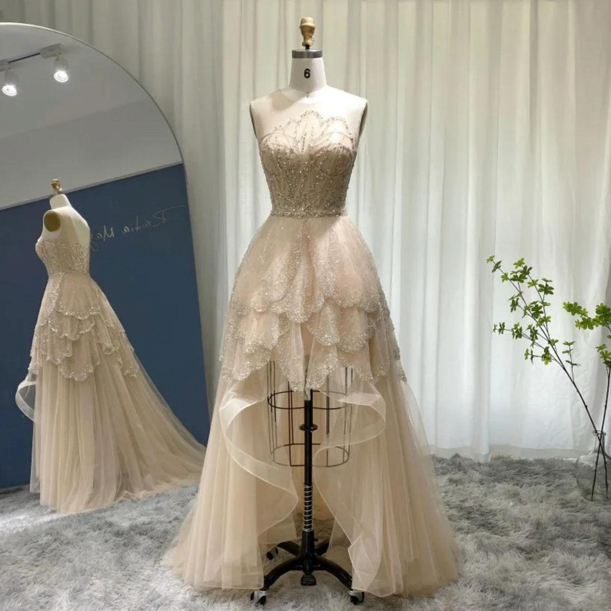 Champagne high-low gown with beaded bodice, tiered tulle ruffles, and a dramatic train on a dress form.