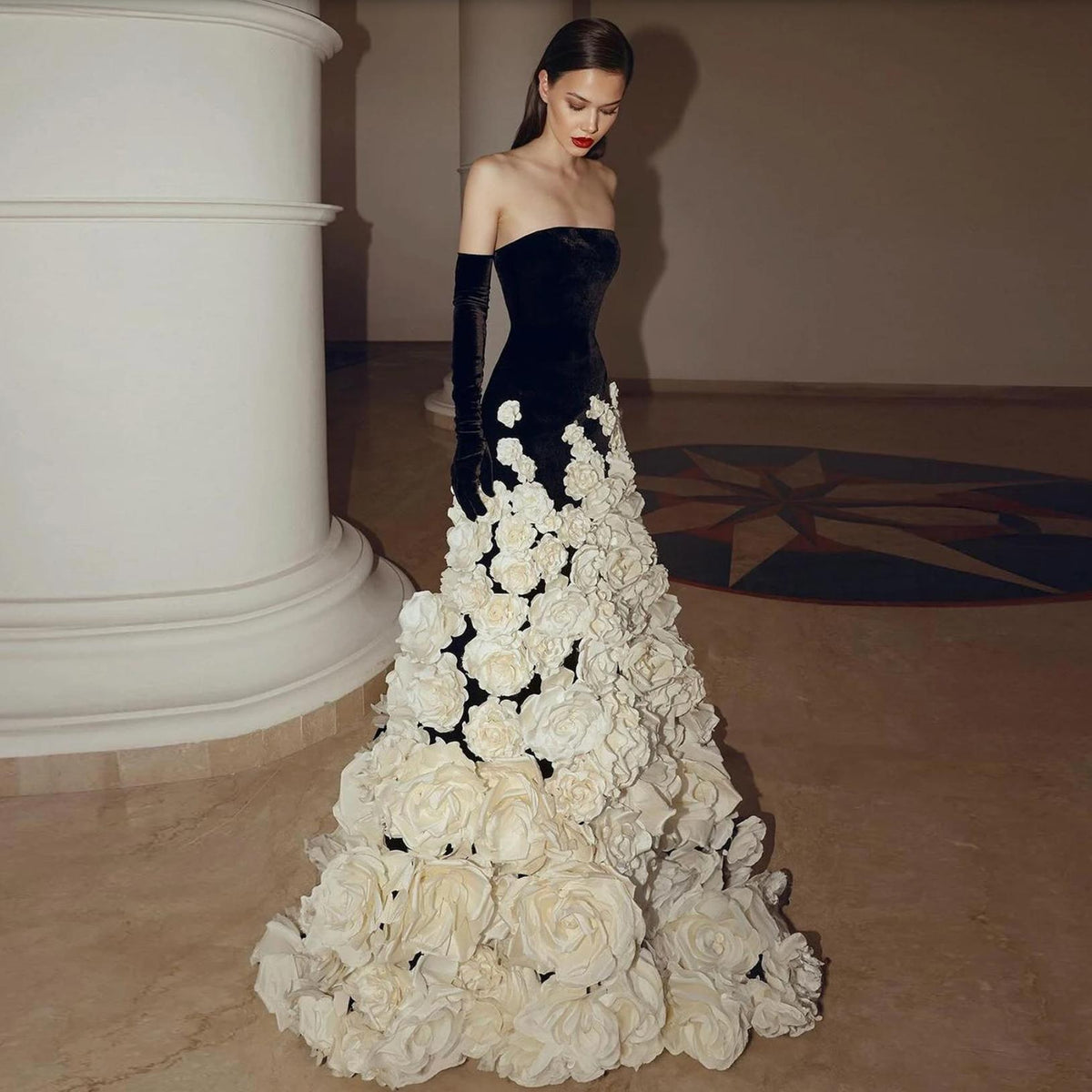 Strapless black velvet evening gown featuring a voluminous skirt adorned with intricate 3D white floral embellishments.