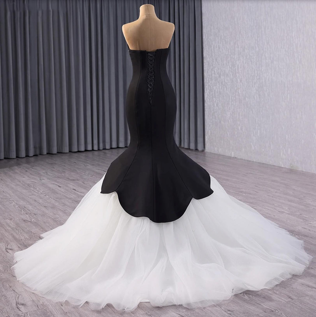 Black velvet fishtail gown with a lace-up back and voluminous white tulle train on a mannequin.