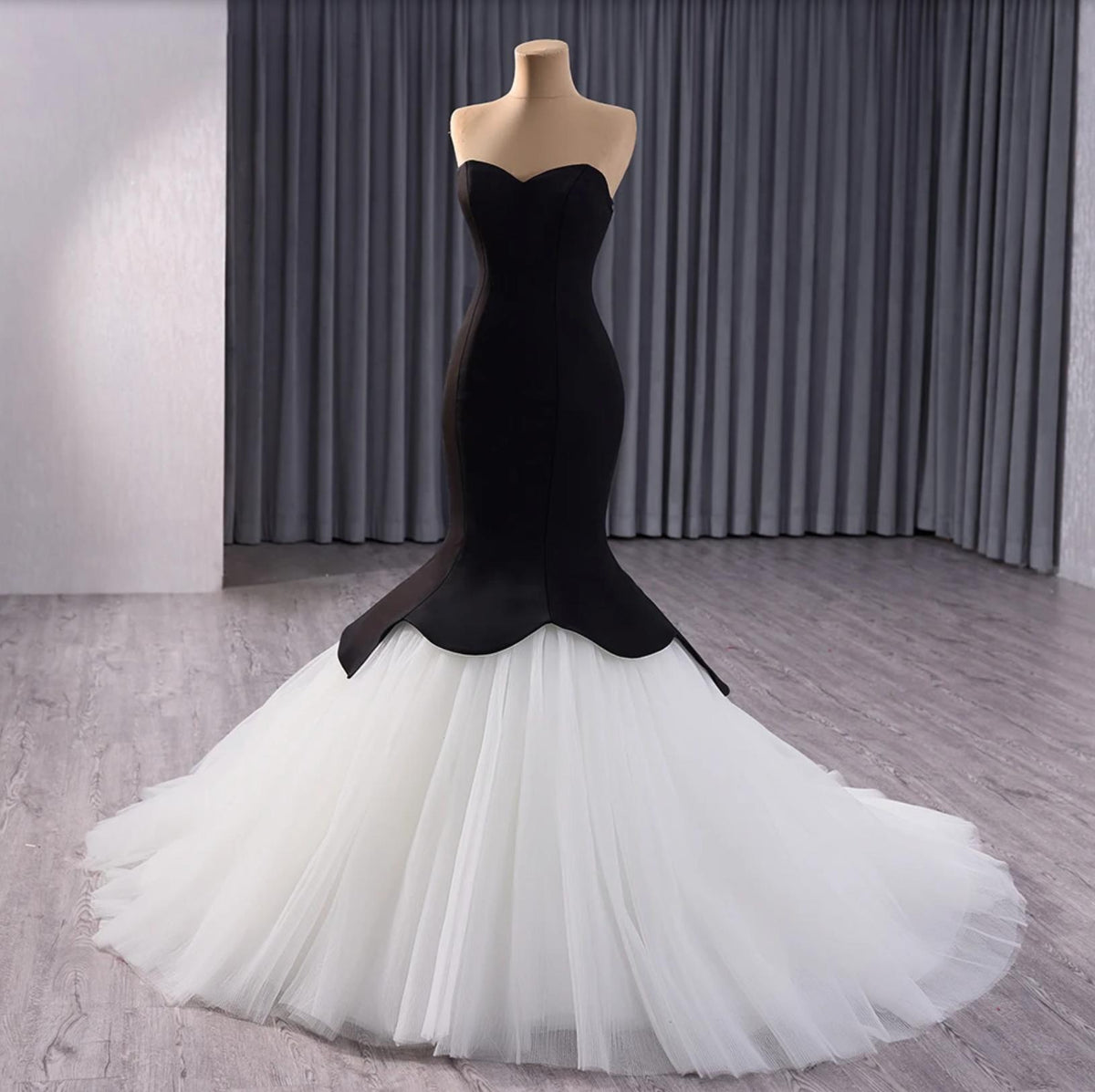 Sleeveless black velvet fishtail gown with a voluminous white tulle skirt on a mannequin.