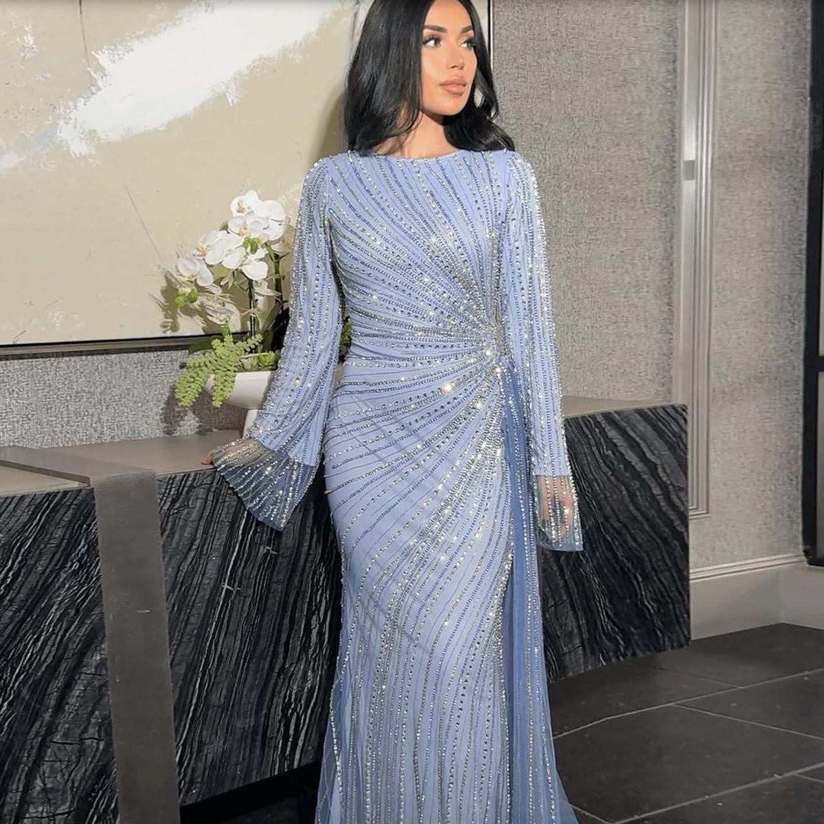 Light blue floor-length evening gown with long sheer sleeves, intricate silver beading, and a side-skirt detail.