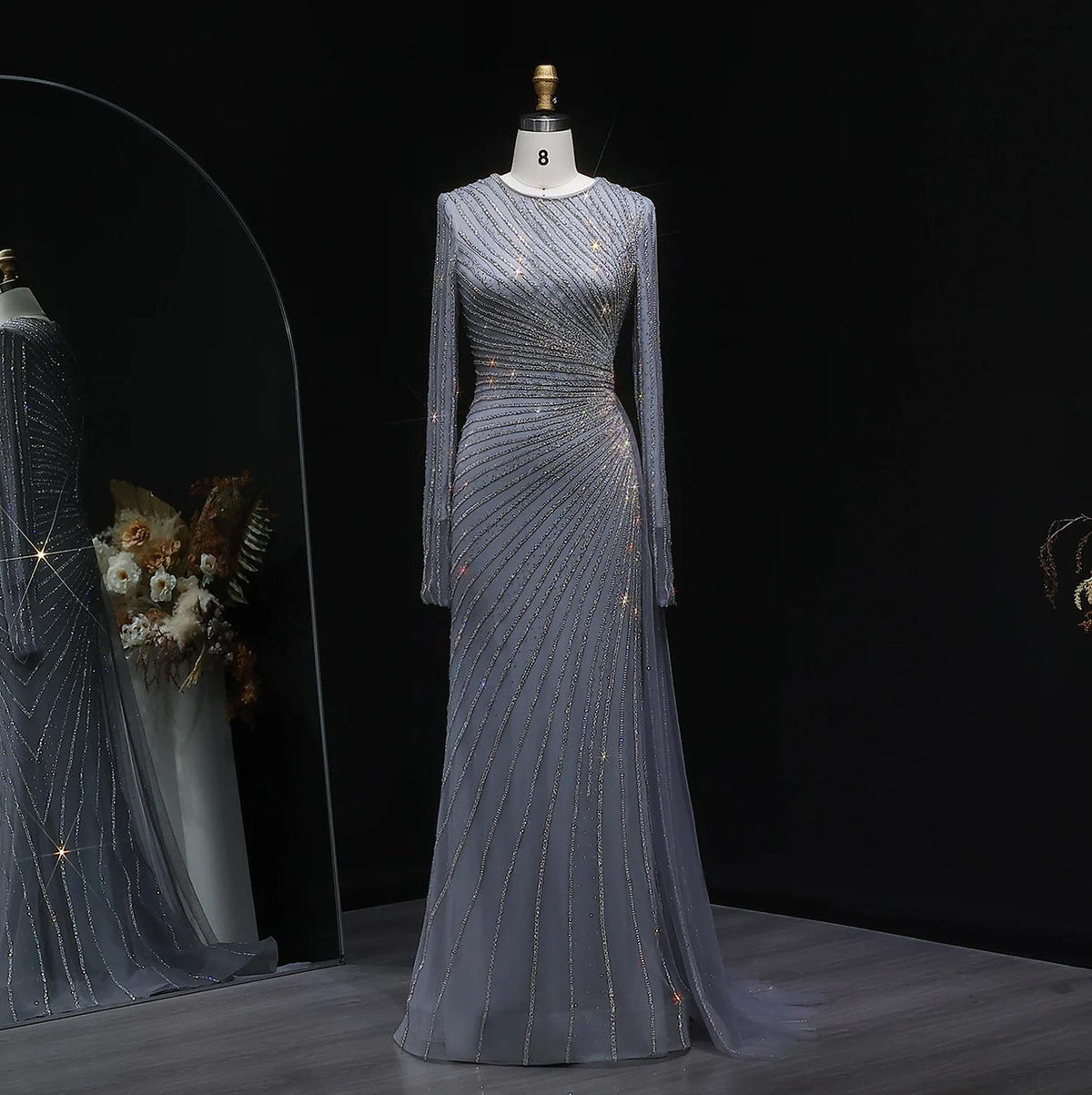 Floor-length grey evening gown with long sheer sleeves, intricate diagonal beaded patterns, and a sweeping train.
