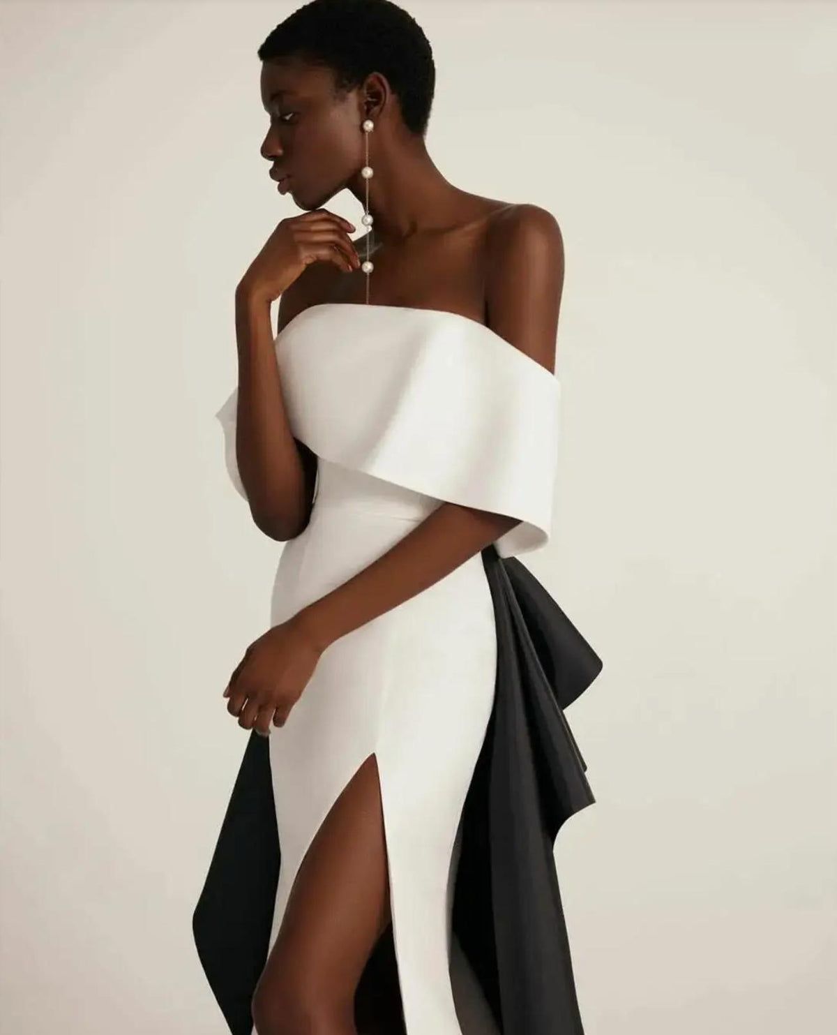 Off-shoulder white satin trumpet gown with a high leg slit and dramatic black train detail.