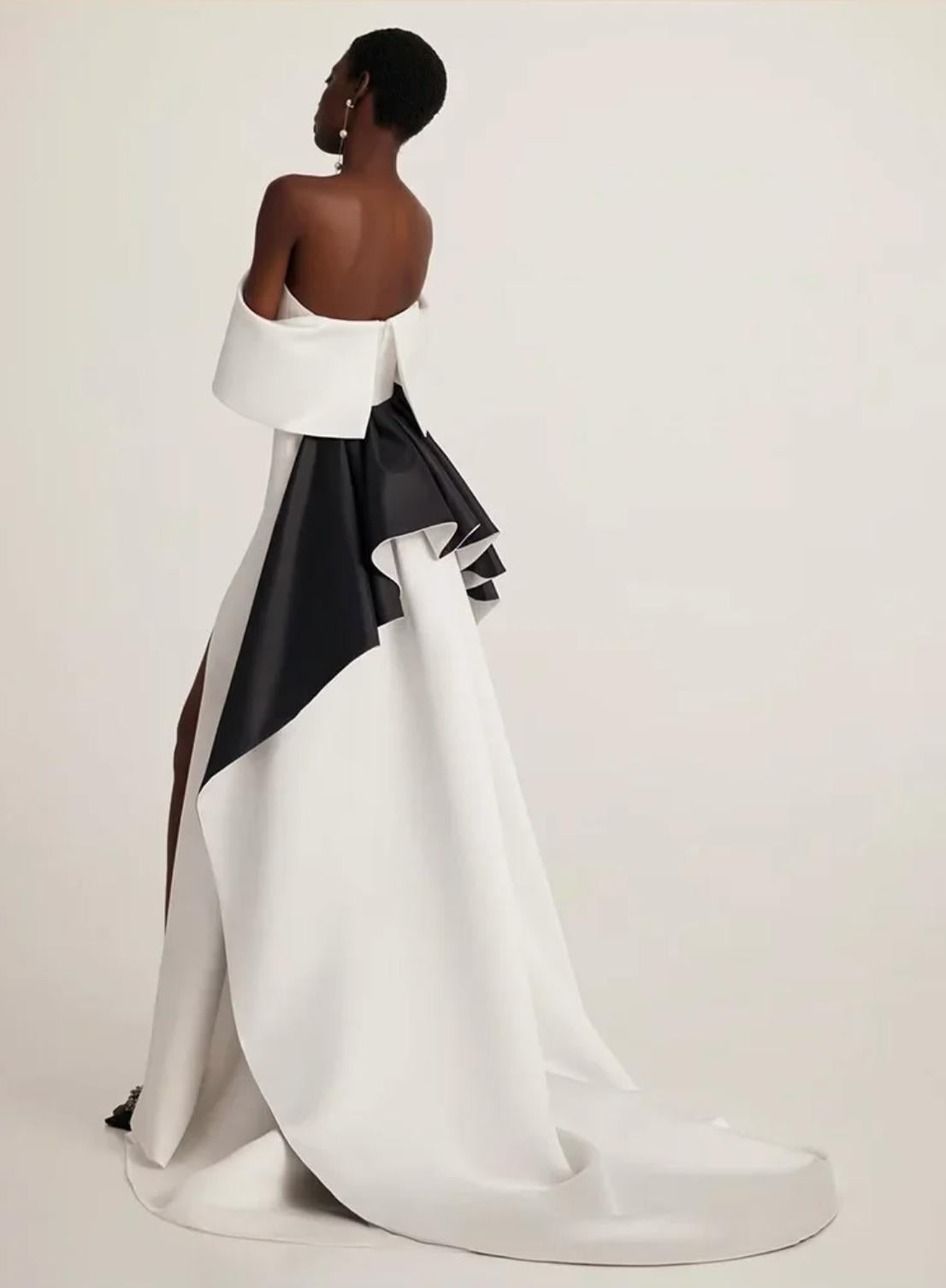 Off-shoulder white and black satin trumpet gown with a dramatic train and elegant floor-length silhouette.