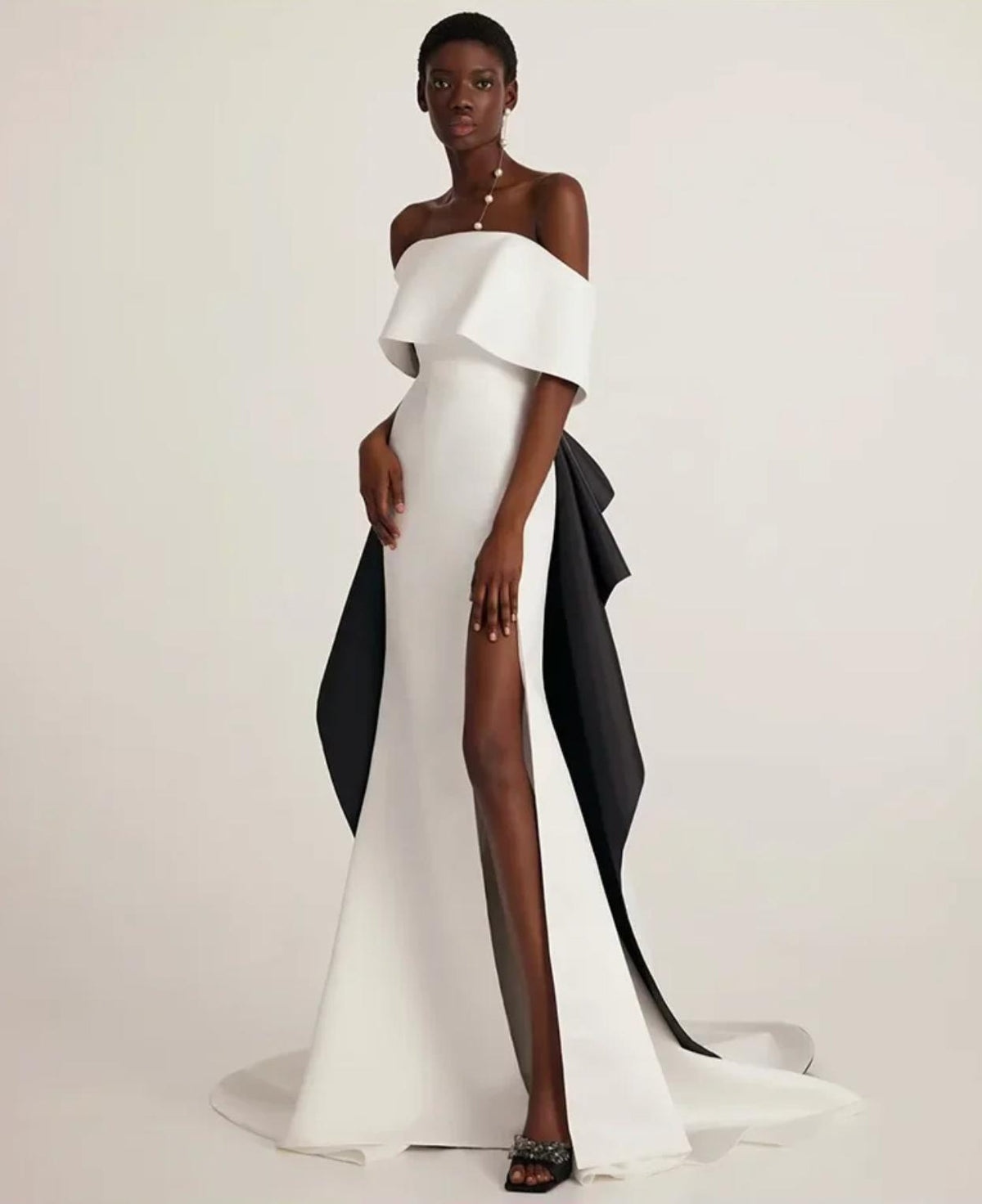 White off-shoulder Hvar gown with a black train, trumpet silhouette, and high leg slit in smooth satin and polyester.