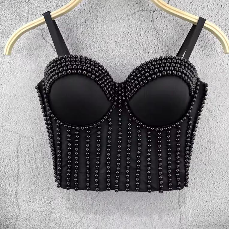 Black corset camisole featuring vertical beaded embellishments and molded cups, hanging on a hanger against a grey wall.