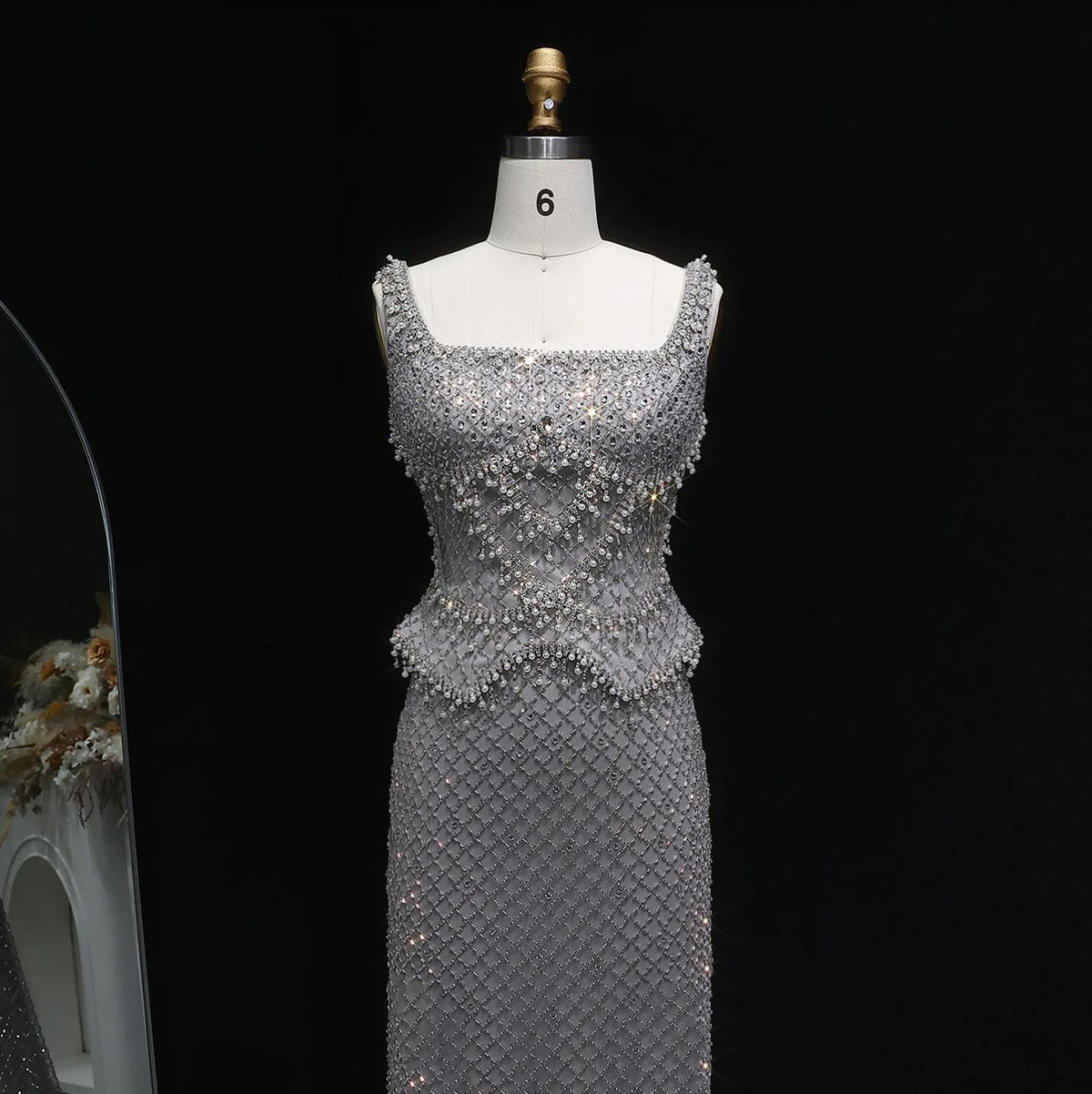 Silver mermaid gown with a square neckline, intricate crystal beading, and a shimmering lattice pattern on a mannequin.