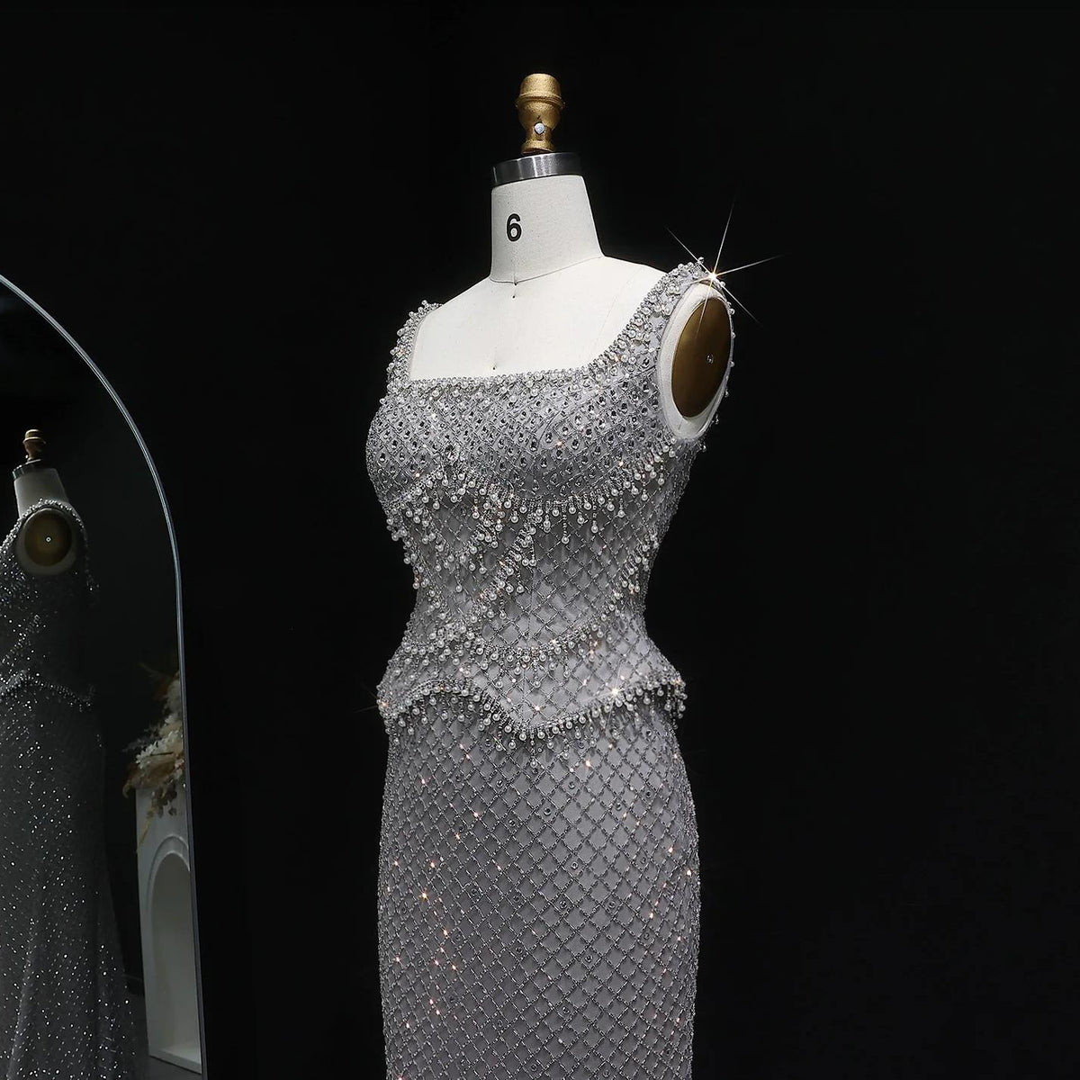 Silver mermaid gown with square neckline, intricate crystal beading, and shimmering lattice detailing on a mannequin.