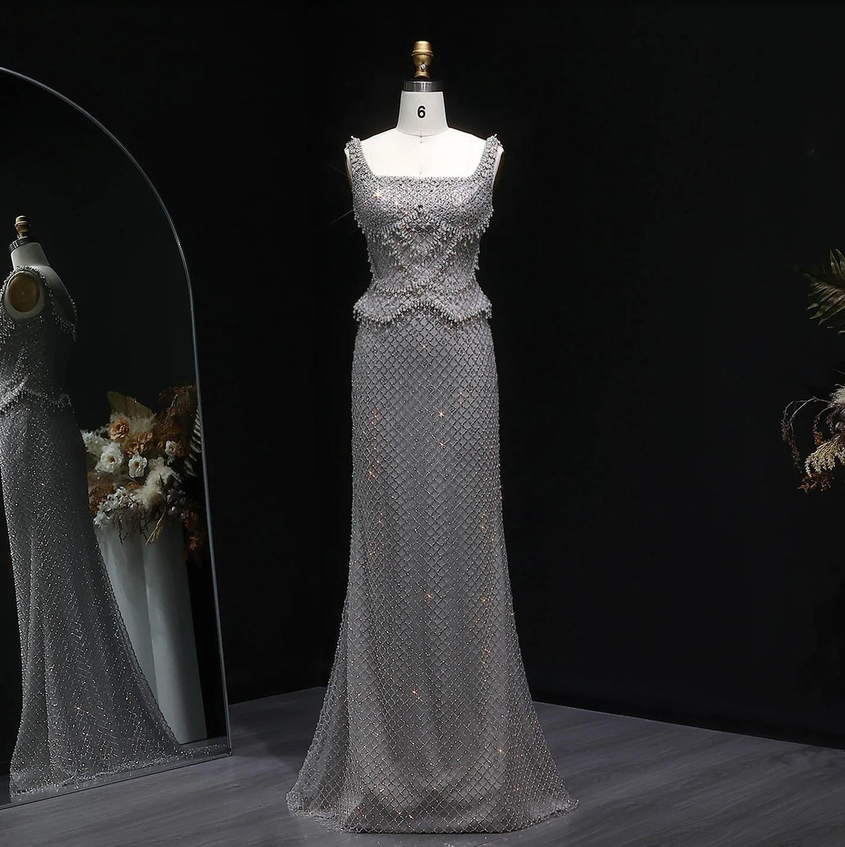 Silver mermaid gown with a square neckline, intricate crystal beading, and a floor-length trumpet silhouette on a mannequin.