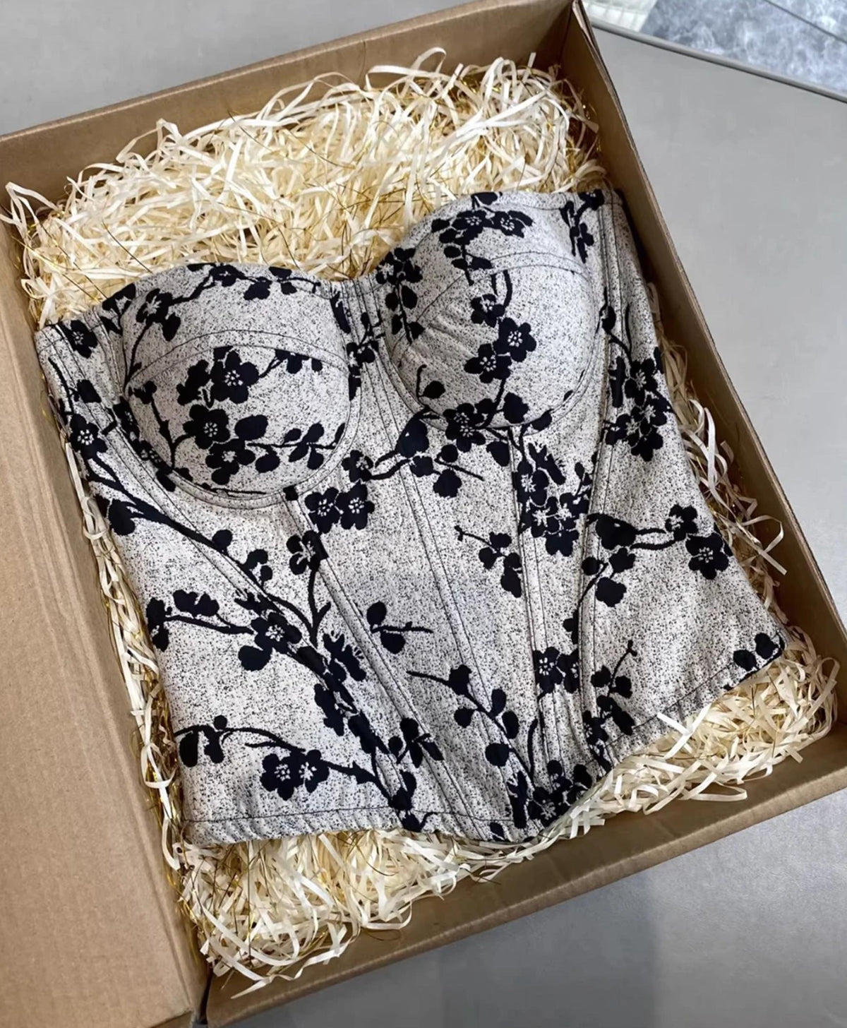 Ivy bustier corset with black floral print on a textured grey background, featuring structured cups in a gift box.