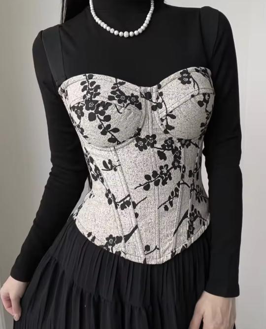 Ivy bustier corset in cream with black floral print, featuring structured cups and steel boning over a black long-sleeve top.