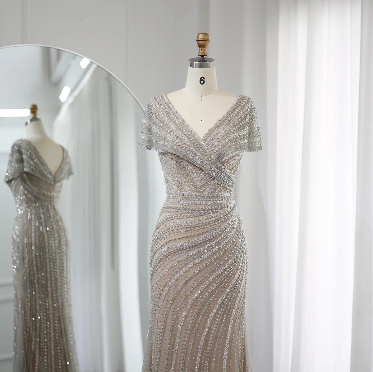 Silver nude mermaid gown with intricate crystal and sequin beading, featuring a V-neck and cap sleeves on a mannequin.