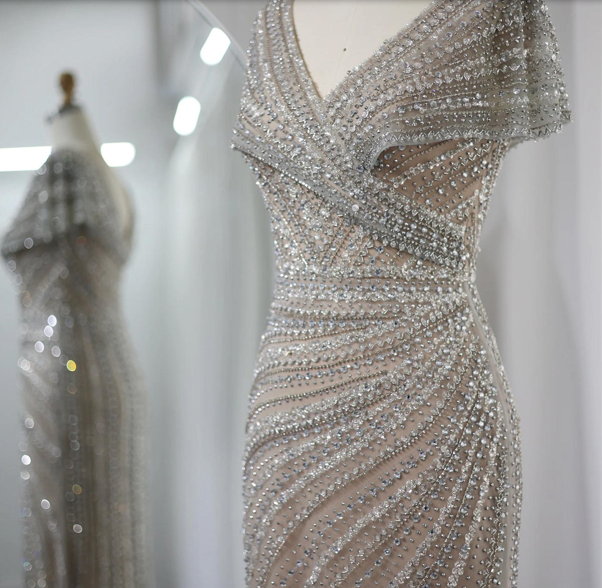 Silver nude mermaid gown with intricate crystal, sequin, and bead embellishments on a plunging V-neck silhouette.