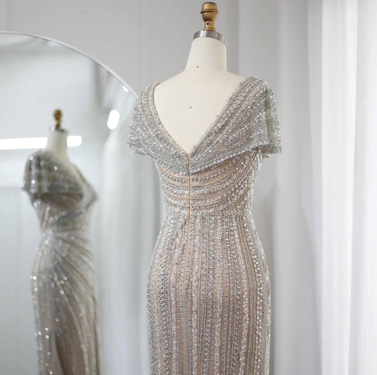 Silver nude mermaid gown on a mannequin, featuring intricate crystal and sequin beadwork with a V-neck and short sleeves.