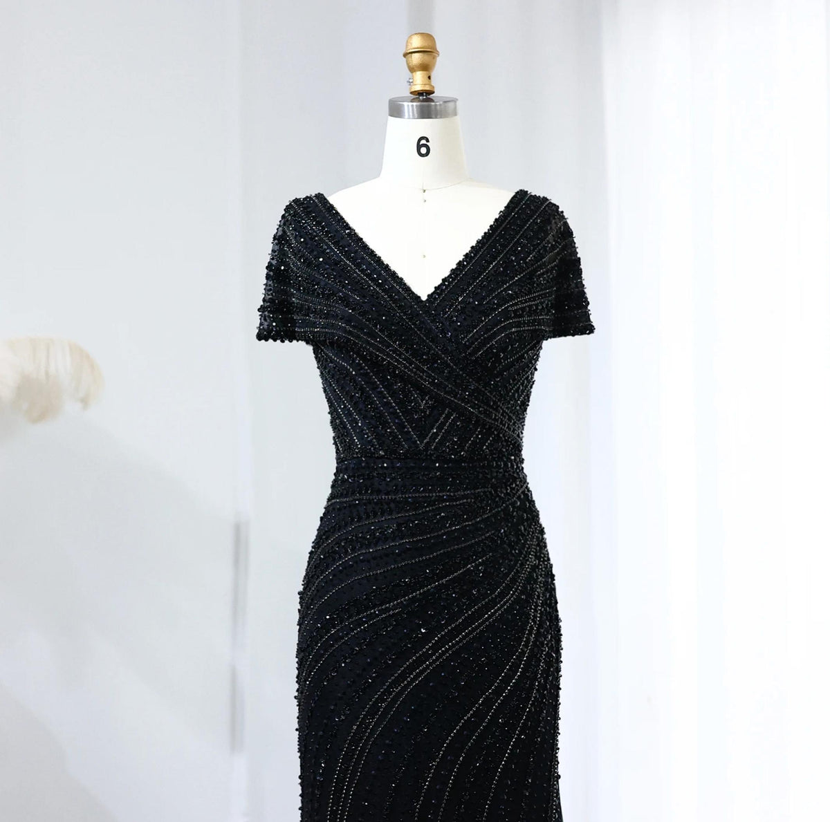 Black mermaid gown with V-neck, short sleeves, and intricate crystal and sequin beadwork on a dress form.