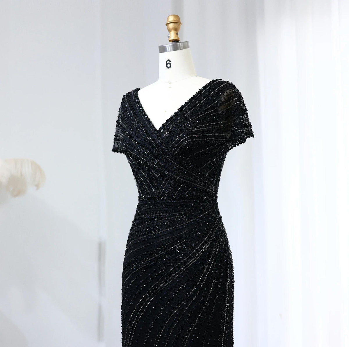 Black mermaid gown with V-neck, short sleeves, and intricate crystal and sequin beadwork on a dress form.