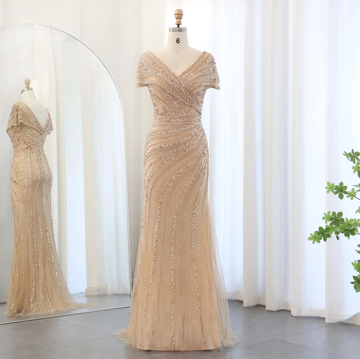 Silver nude mermaid gown with a plunging V-neck, intricate crystal beading, and sequin appliqués on a mannequin.
