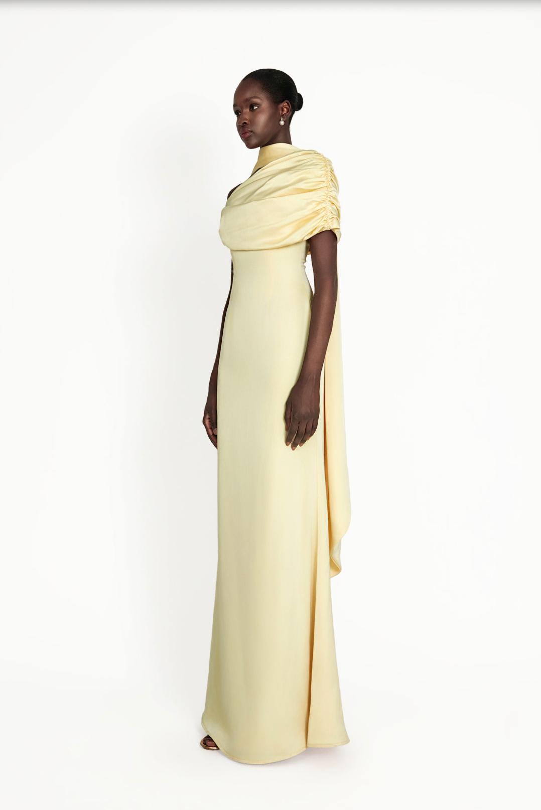 Model wearing a pale yellow satin Kulture dress with a gathered Bardot neckline and flowing A-line silhouette.