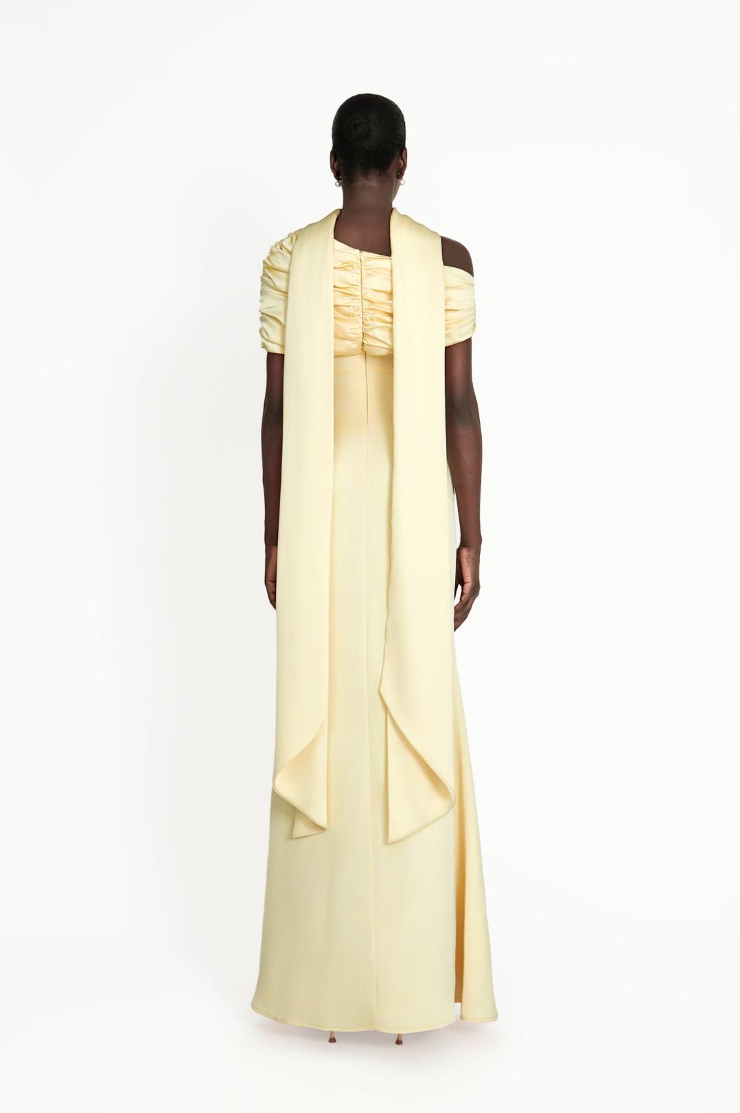 Back view of a pale yellow satin Kulture dress with a gathered Bardot neckline and long, flowing shoulder drapes.