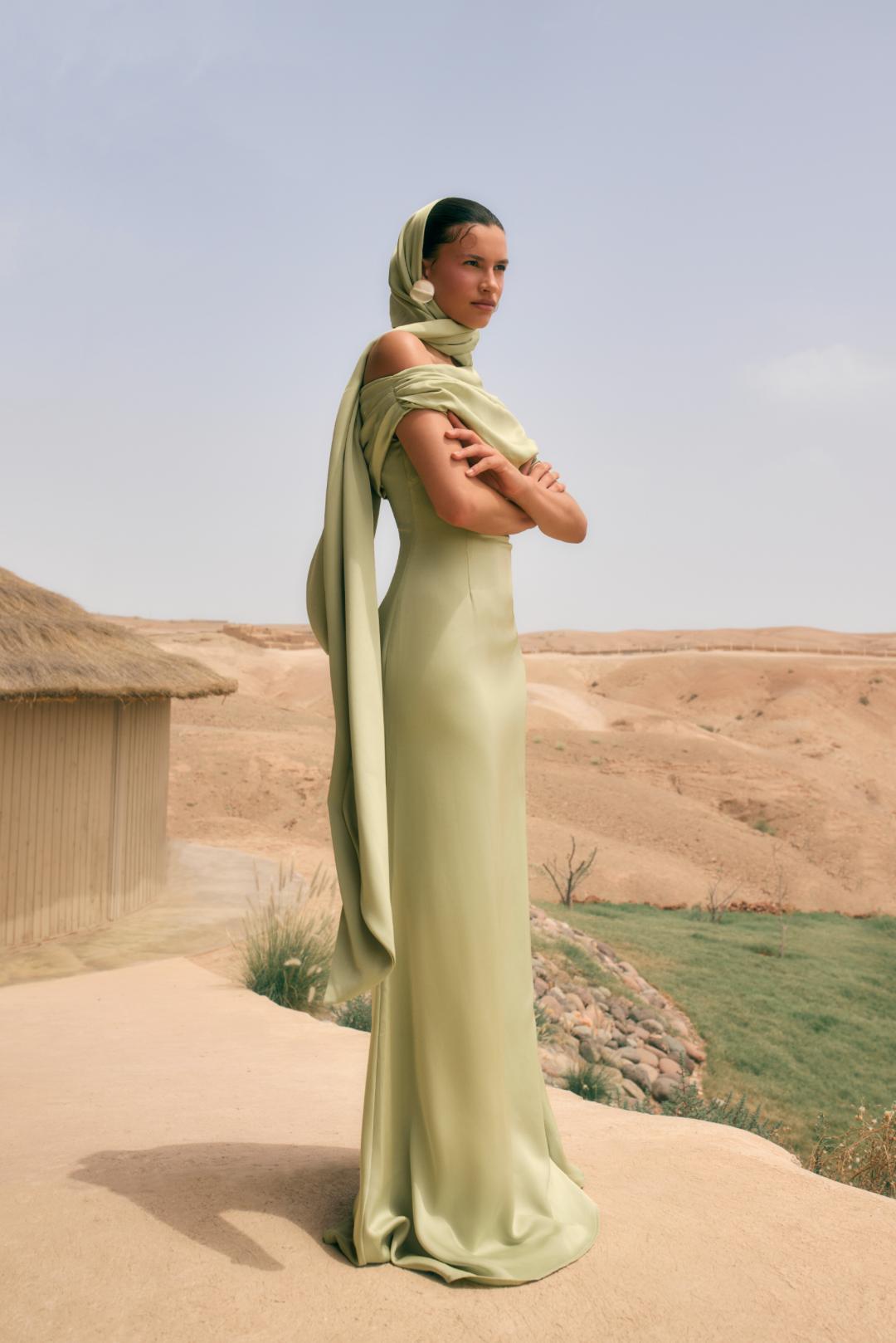 Sage green satin Kulture dress with a gathered Bardot neckline and flowing A-line silhouette, worn with a matching headscarf.