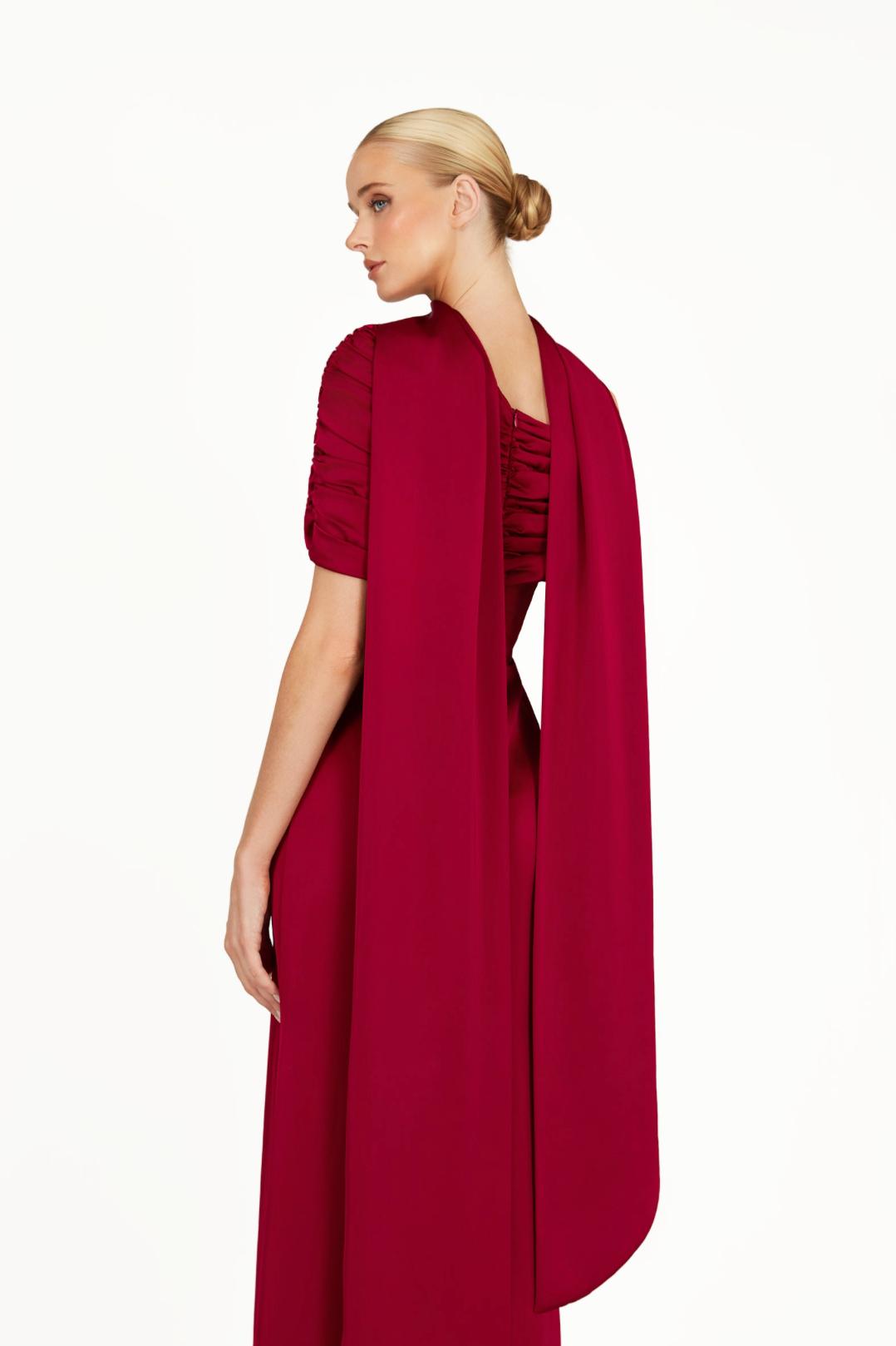 Model wearing a deep red satin Kulture dress with a gathered Bardot neckline and flowing A-line silhouette.