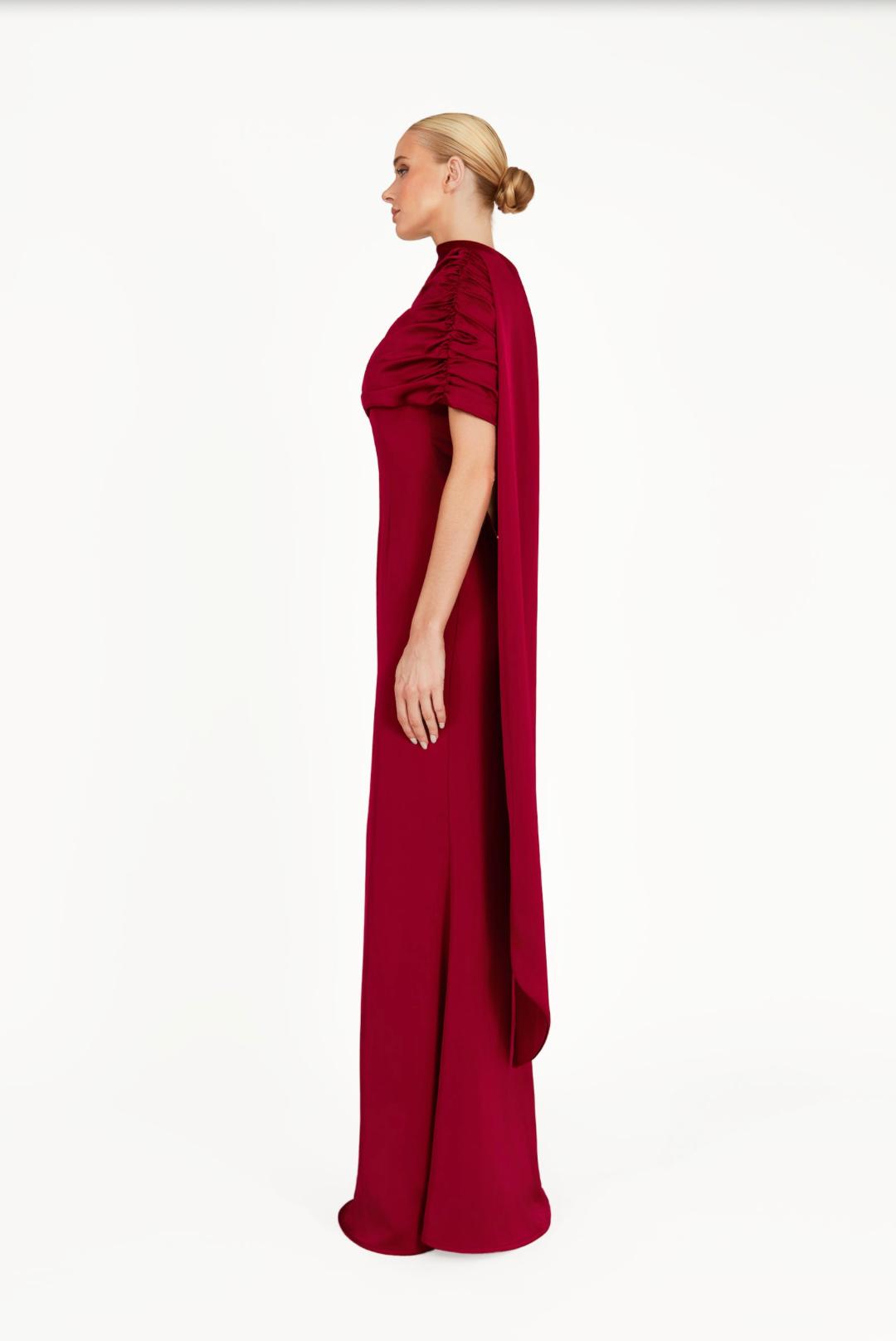 Side profile of a woman wearing a floor-length, deep red satin A-line gown with a gathered Bardot neckline.