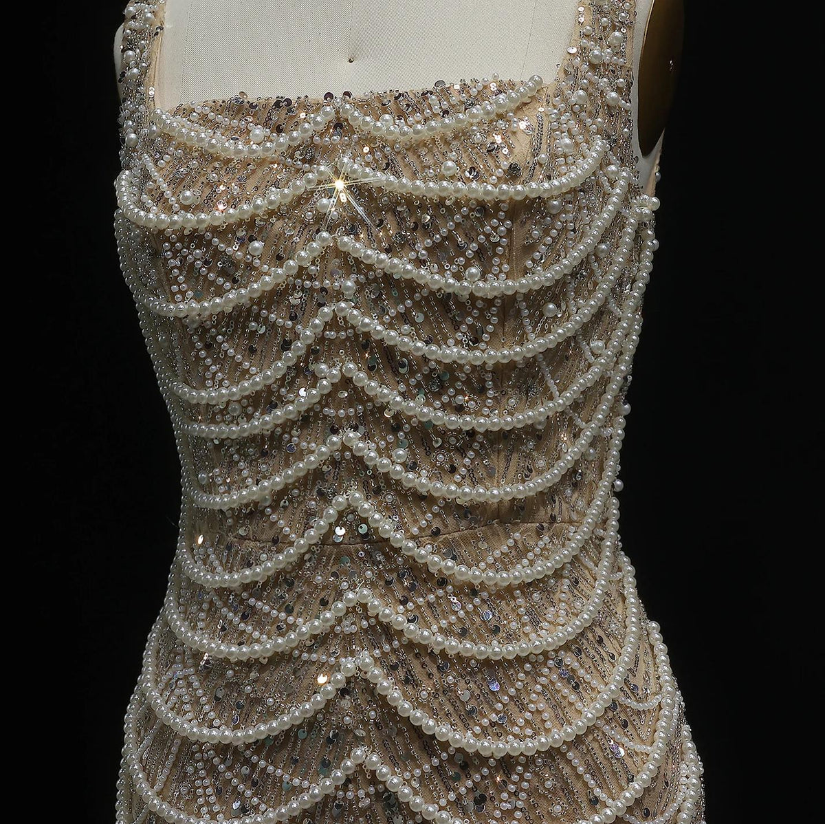 Nude sleeveless gown featuring intricate pearl draping, shimmering sequins, and a scoop neckline on a mannequin.