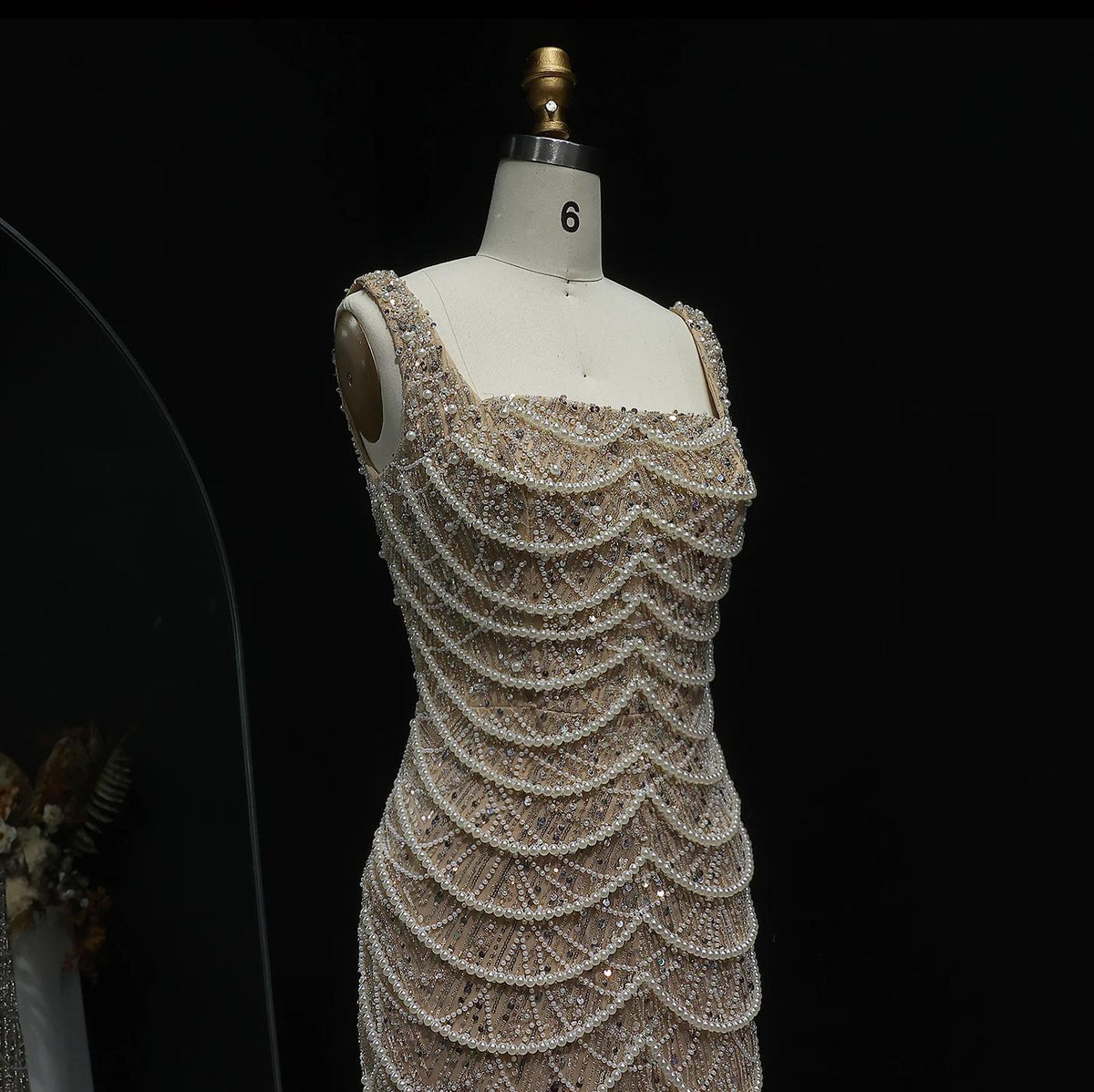 Nude floor-length sheath gown with a scoop neckline, adorned with intricate pearl draping and sparkling beadwork.