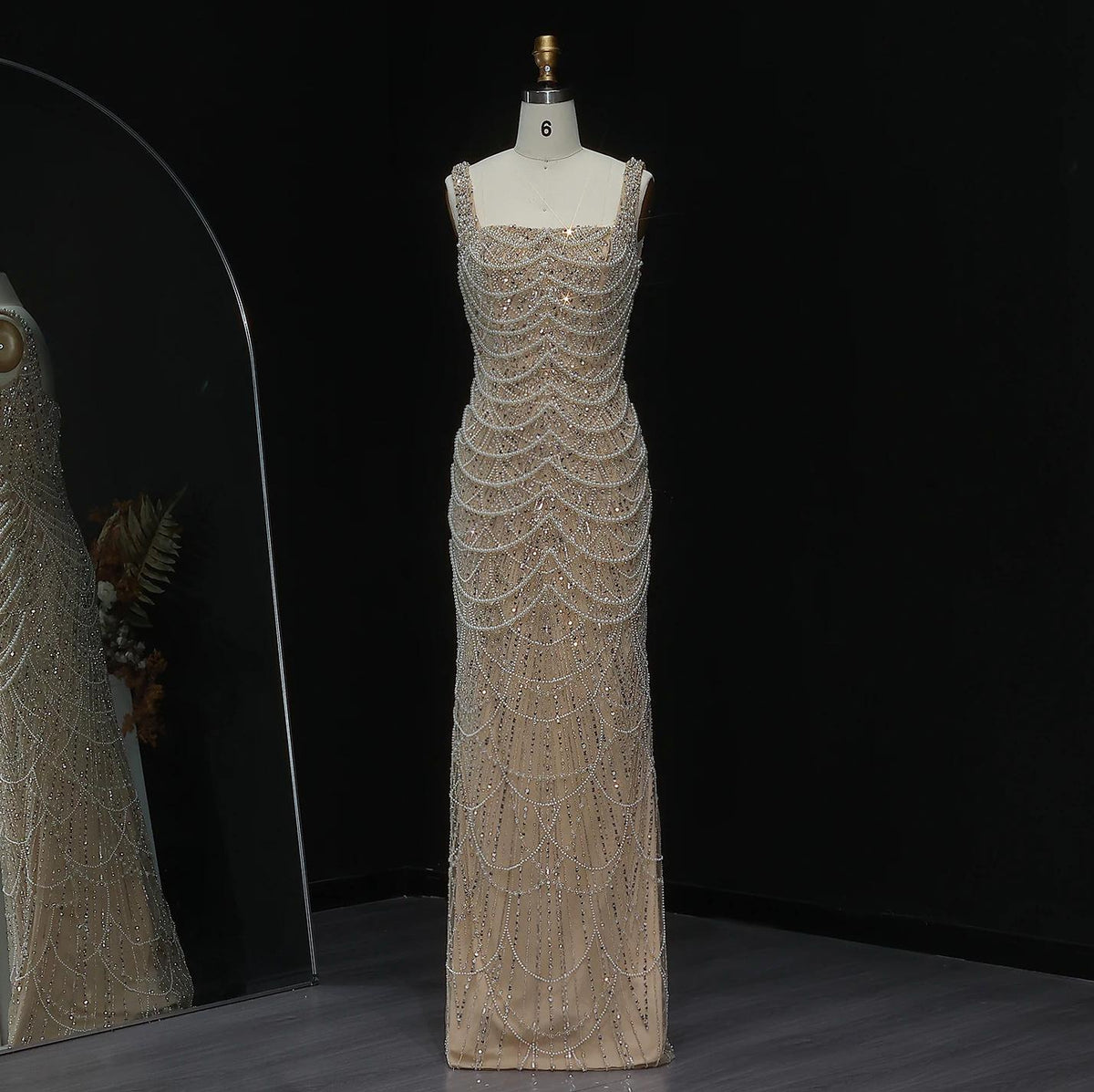 Nude floor-length sheath gown with a scoop neckline, adorned with intricate pearl and crystal beading in a draped pattern.