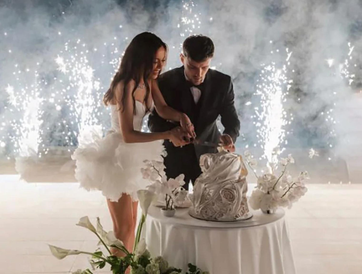 Woman wearing a white tulle mini party dress with floral details and a sweetheart neckline cutting a wedding cake.