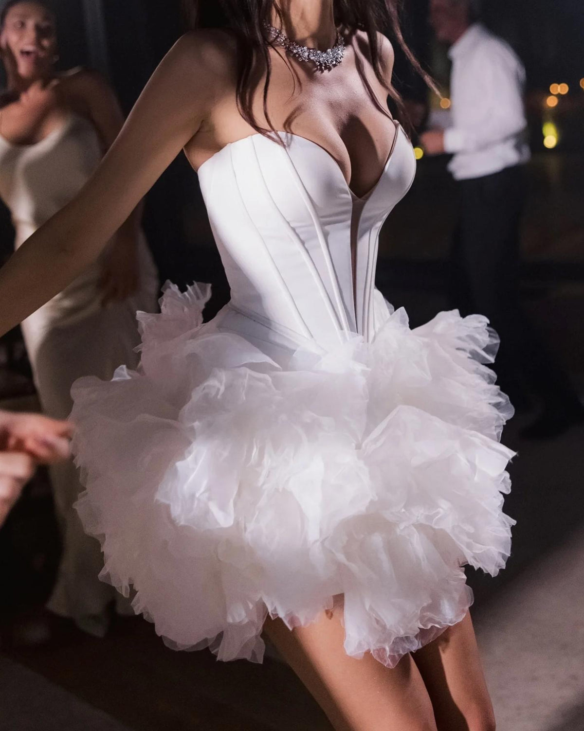 White mini party dress with a structured sweetheart bodice and voluminous ruffled tulle skirt at a night event.