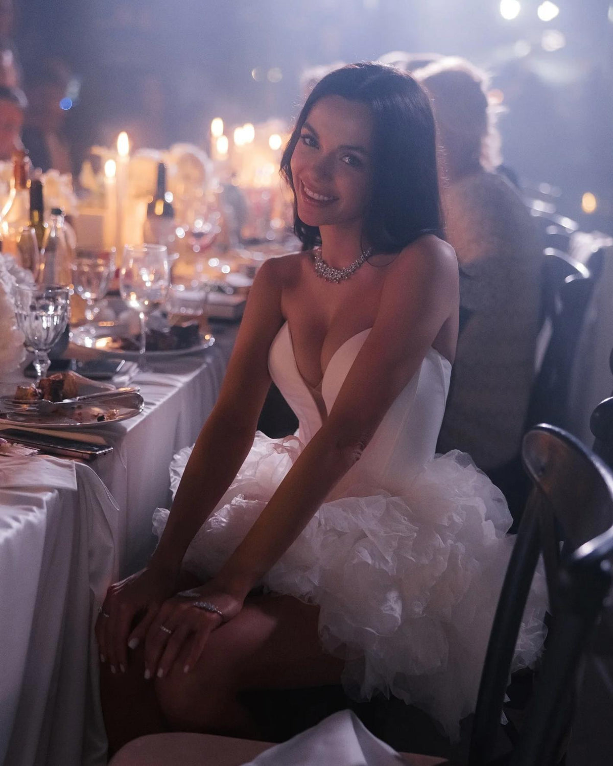 Woman wearing a white mini party dress with a sweetheart neckline and voluminous tulle skirt at a candlelit dinner.