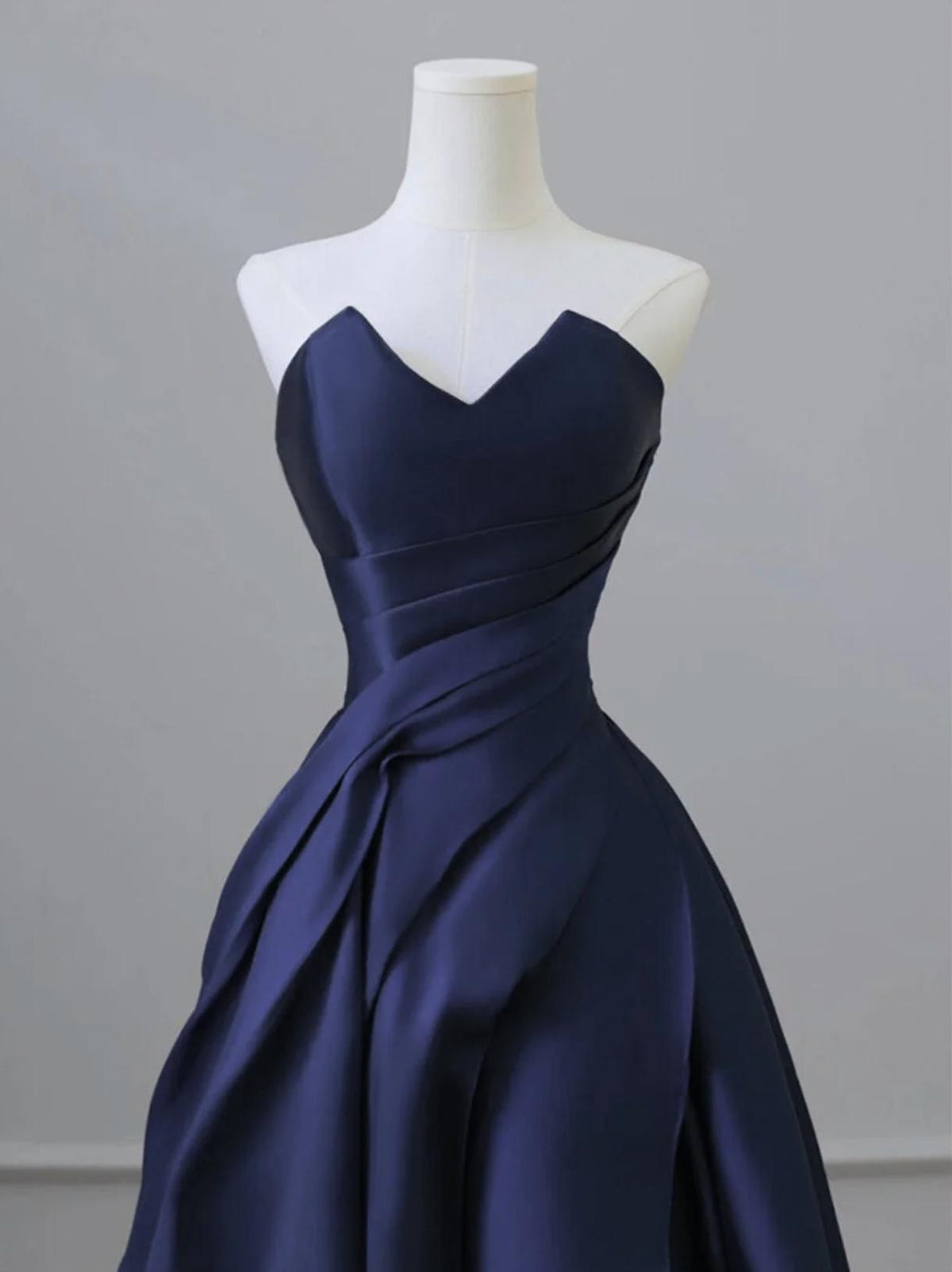 Elegant navy blue satin A-line gown with a sweetheart neckline and draped bodice on a mannequin.